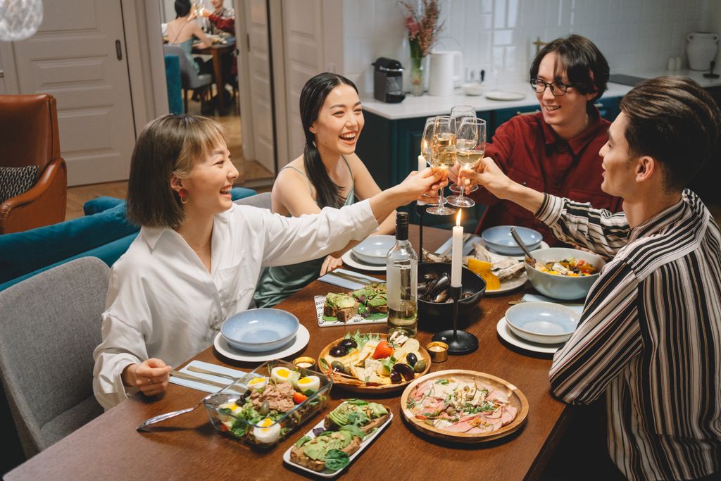 A lively gathering of friends sharing a meal, raising wine glasses in a cheerful indoor setting.