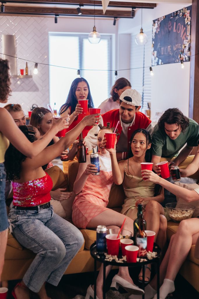 Lively group of young adults cheering with drinks at an indoor apartment party.